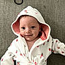 Estella is registered to the contest to win money with this photo: baby, child, hooded_robe, strawberry_pattern, smile, couch, fabric, earrings, hair_tie, infant, white_clothing, pink_lining, cute, portrait, indoor, relaxed, small_face, soft_texture, happy, person
