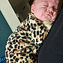 baby, infant, sleeping_baby, leopard_print, onesie, parent, holding, cuddling, indoor, home, portrait, face, cheek, head, closed_eyes, cozy, soft_lighting, hand, doorway, smoke_detector