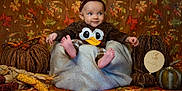 Avah is registered to the contest to win money with this photo: baby, child, costume, duck, brown_clothing, headband, blanket, autumn, fall_leaves, decorations, pumpkins, corn, woven_pumpkins, smile, portrait, indoor, seasonal, cute, sitting, cozy
