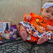 Avah joined the competition — help win amazing prizes! baby, child, halloween, orange_clothing, headband, white_bow, couch, skull_decorations, purple_jar, black_spider, decorations, sign, pumpkins, black_cat, fabric, foot, hand, cute, portrait, holiday