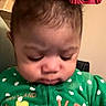 baby, child, green_clothing, polka_dot, face, indoor, lamp, video_call, curly_hair, person, expression, sitting, portrait, young_child, technology, communication, casual, home, cute, infant
