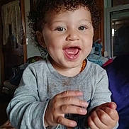 Destinee joined the competition — help win amazing prizes! toddler, child, curly_hair, smiling, happy, indoor, clapping, sweatshirt, person, portrait, cute, baby, expression, hands, seated, cozy, home, window, furniture, casual