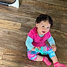 baby, bright_colors, casual_clothing, child, colorful_pants, curly_hair, cute, flooring, hair_pick, happy, indoors, person, pink_shirt, playful, portrait, sitting, smiling, sock, toddler, wooden_floor