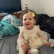 Destinee joined the competition — help win amazing prizes! baby, child, smile, dress, headband, bow, bed, blanket, television, furniture, indoors, person, cute, happy, sitting, sock, curly_hair, toy, room, toddler