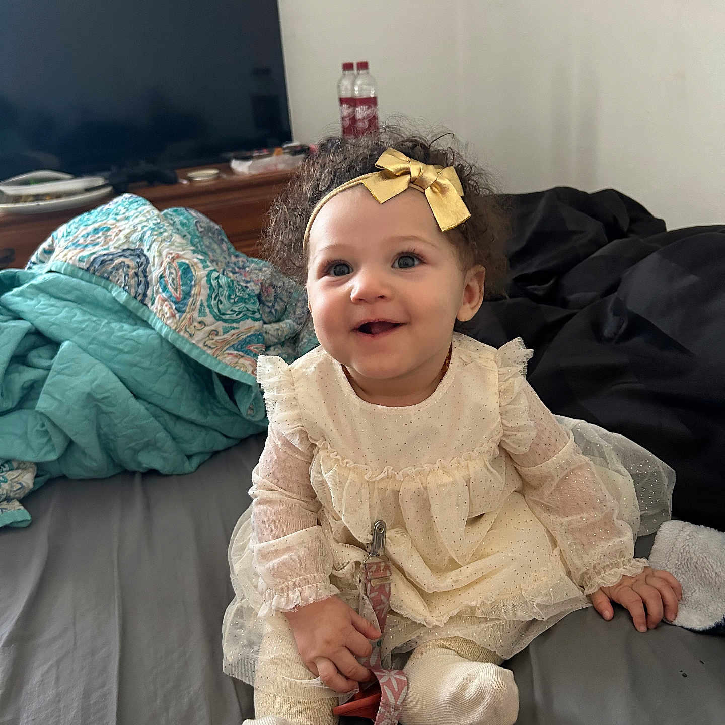 Destinee joined the competition — help win amazing prizes! baby, bed, blanket, bow, child, curly_hair, cute, dress, furniture, happy, headband, indoors, person, room, sitting, smile, sock, television, toddler, toy