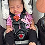 baby, sleeping, car_seat, curly_hair, pink_shirt, black_pants, bare_feet, infant, child, safety_harness, padded_seat, warning_label, indoors, cute, peaceful, resting, young_child, toddler, seatbelt, child_safety