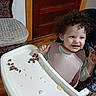 baby, bib, chair, child, clothing, curly_hair, cushion, feeding, flooring, food, happy, high_chair, indoor, person, playful, room, smile, toddler, tray, wooden_door