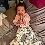 baby, bed, blanket, butterfly_pattern, child, clip, cozy, curious, curly_hair, cute, face, gray_sheets, indoor, infant, lying_down, pacifier, pants, person, pink_clothing, socks