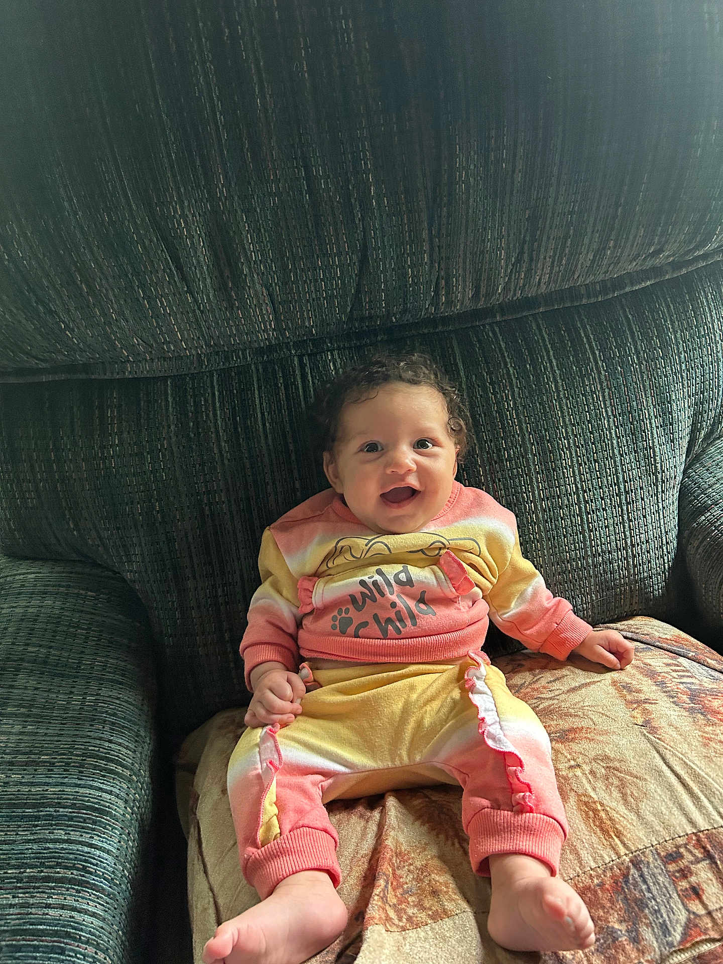 Destinee is registered to the contest to win money with this photo: baby, child, smiling, sitting, couch, clothing, happy, infant, person, indoors, cute, pattern, fabric, foot, hand, face, home, portrait, cozy, colorful