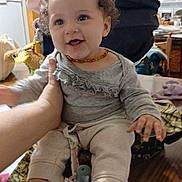 Destinee joined the competition — help win amazing prizes! amber_necklace, baby, background, child, clothing, cozy, curly_hair, cute, face, furniture, hand, happy, home, indoors, pacifier, person, sitting, smiling, table, toy
