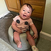 Daniella joined the competition — help win amazing prizes! baby, baby_seat, cabinet, carpet, child, cute, face, floor_tile, furniture, happy, home, indoor, infant, person, pink_shirt, seat, sitting, smile, sock, wooden_cabinet