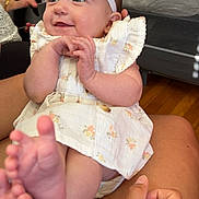Arielle joined the competition — help win amazing prizes! baby, infant, smiling, headband, white_bow, floral_dress, barefoot, toes, hands, legs, person, holding, indoor, crib, patterned_fabric, wooden_floor, skin, happy, child, portrait