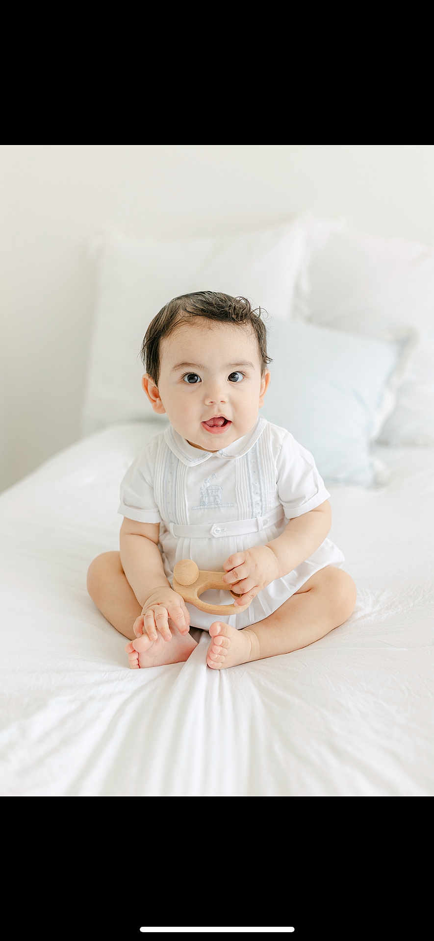 Ryan is registered to the contest to win money with this photo: baby, child, infant, white_bed, wooden_toy, curious, cute, sitting, indoors, minimalistic, pillow, soft_lighting, portrait, clothing, person, smile, hands, feet, young, happy