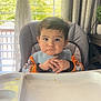 toddler, child, high_chair, bib, indoor, window, curtains, hands, face, hair, clothing, expression, food_tray, baby_toys, home, furniture, plant, table, daylight, portrait