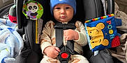 Ezra is registered to the contest to win money with this photo: baby, infant, car_seat, blue_hat, nike, onesie, football_pattern, toy, blanket, safety_harness, child, indoor, cute, serious_expression, plush_toy, colorful, seat, holding, young_child, portrait