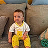 toddler, child, baby, sitting, yellow_pajamas, winnie_the_pooh, couch, pillows, toy, indoor, cute, face, feet, clothing, expression, home, relaxed, person, childhood, playful