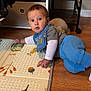 baby, child, floor, play_mat, blue_pants, gray_shirt, socks, wooden_floor, indoor, curious, lying_down, person, home, toy, crawling, face, head, expression, clothing, baby_bib