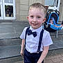 baby, blond_hair, bow_tie, boy, building, car_seat, child, door, footwear, glass, happy, outdoor, pavement, person, reflection, shorts, smiling, stairs, suspenders, white_shirt
