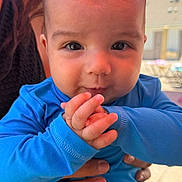 Isaiah is registered to the contest to win money with this photo: baby, child, infant, blue_shirt, red_shorts, hands, outdoor, sunny, umbrella, adult_hand, playful, cheeks, face, person, summer, daylight, smiling, closeup, portrait, background