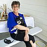 black_pants, blue_top, casual, companion, concrete_floor, dog, dried_plants, glasses, happy, leash, outdoor, pet, portrait, seated, smile, table, vase, white_bench, woman, yellow_hose