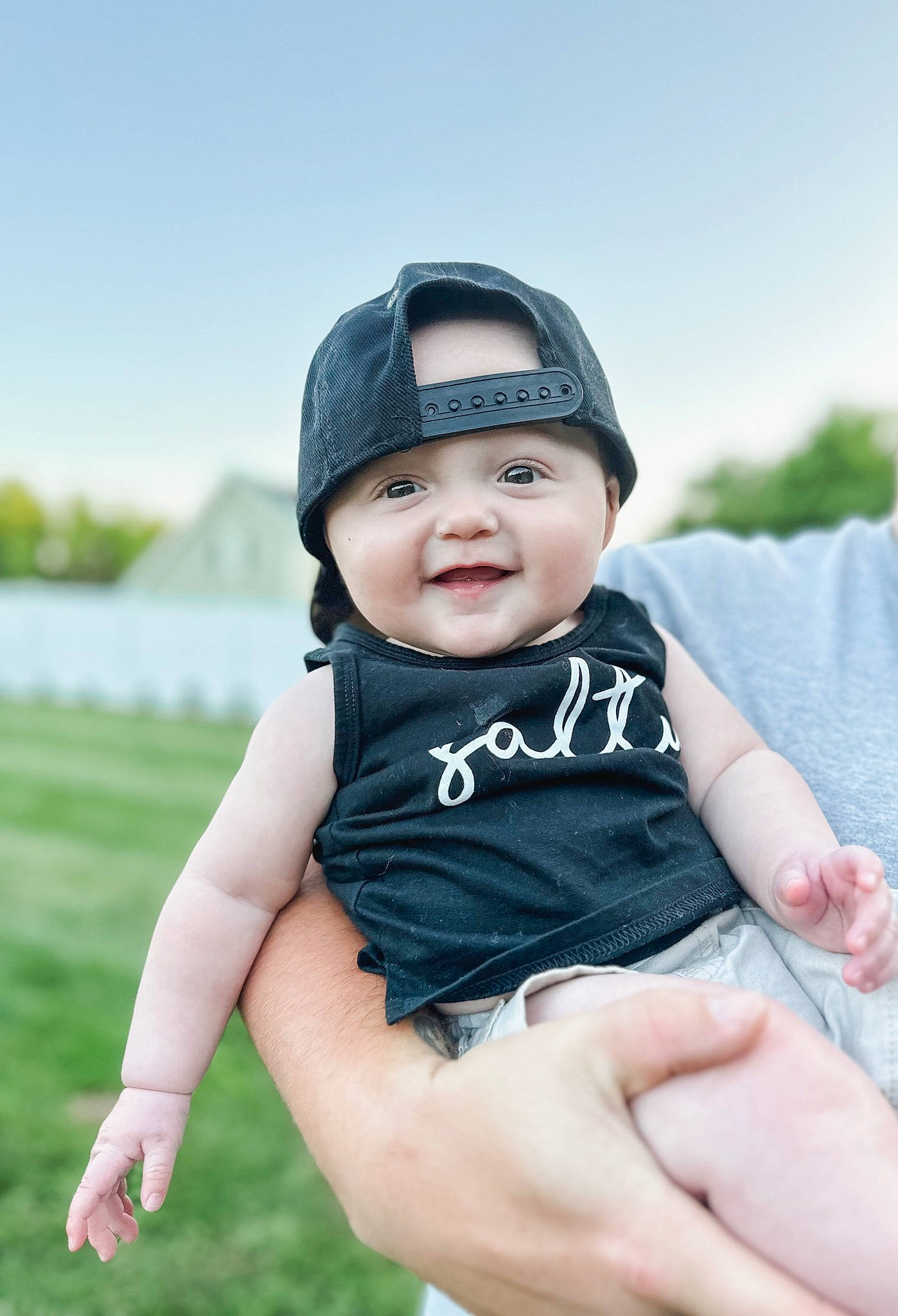 Clayton is registered to the contest to win money with this photo: arm, baby, baby_toddler_clothing, baseball_cap, cap, child, electric_blue, flash_photography, gesture, grass, hand, happy, hat, headwear, leisure, people_in_nature, person, recreation, sitting, sky
