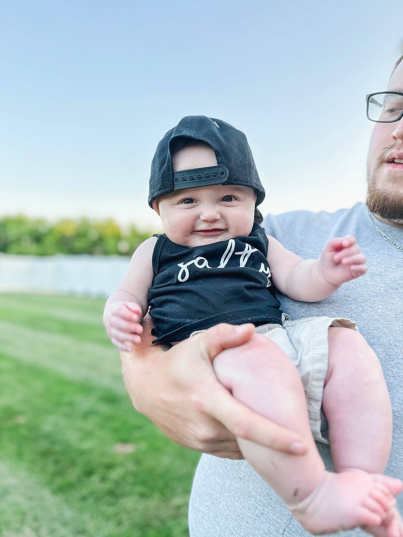 Clayton is registered to the contest to win money with this photo: arm, baby, baby_toddler_clothing, beard, child, face, flash_photography, fun, gesture, grass, hand, happy, hat, headwear, leisure, person, plant, sitting, skin, sky