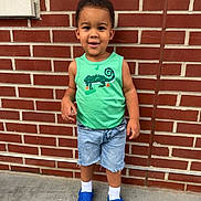 Jaziel joined the competition — help win amazing prizes! child, toddler, boy, smiling, green_tank_top, denim_shorts, blue_crocs, white_socks, brick_wall, outdoor, concrete_floor, standing, casual_clothing, short_hair, happy, cute, portrait, daylight, person, young_child