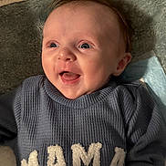 Levi joined the competition — help win amazing prizes! baby, infant, smile, happy, sweater, text_on_clothing, face, eyes, tongue, hand, blanket, soft_texture, lying_down, indoor, portrait, closeup, newborn, skin, head, cheeks