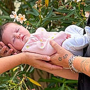 Ilohé a rejoint le concours — aidez-le/la à gagner de superbes lots ! baby, sleeping, hands, tattoo, bracelet, pink_clothing, white_pants, flower, greenery, outdoor, person, infant, peaceful, nature, portrait, closeup, skin, rest, cute, tenderness