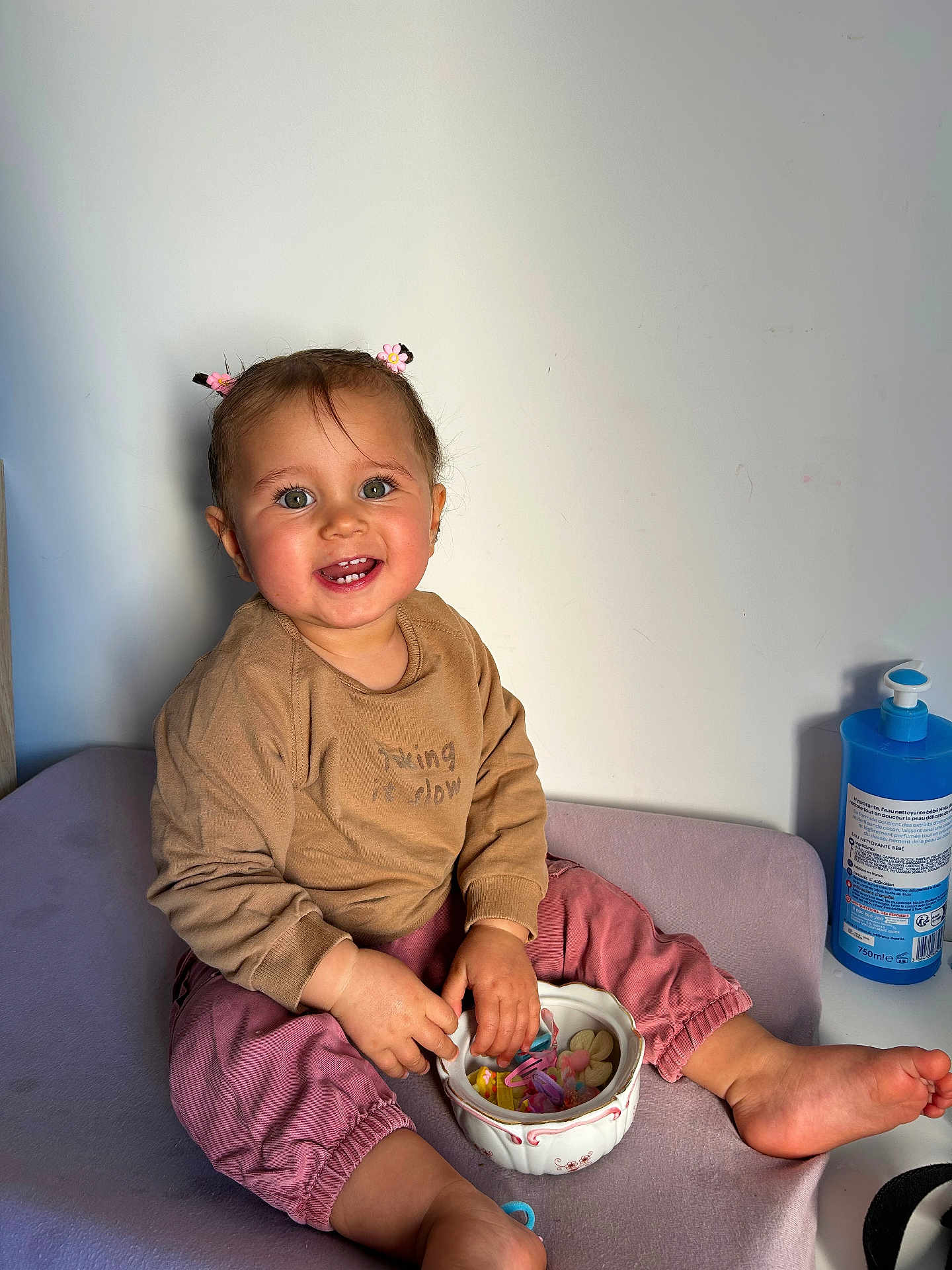 Aliyah participe au concours pour gagner de l'argent avec cette photo : toddler, child, smiling, sitting, hair_accessory, bowl, hair_clips, pink_pants, brown_sweater, barefoot, indoors, light_wall, table, hand, face, cute, happy, playful, skin, person
