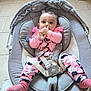 baby, infant, child, pink_clothing, baby_rocker, seatbelt, socks, thumb_sucking, floor_tile, white_shoe, indoor, curious_expression, seated, baby_girl, comfortable, casual, person, portrait, baby_toys, soft_fabric