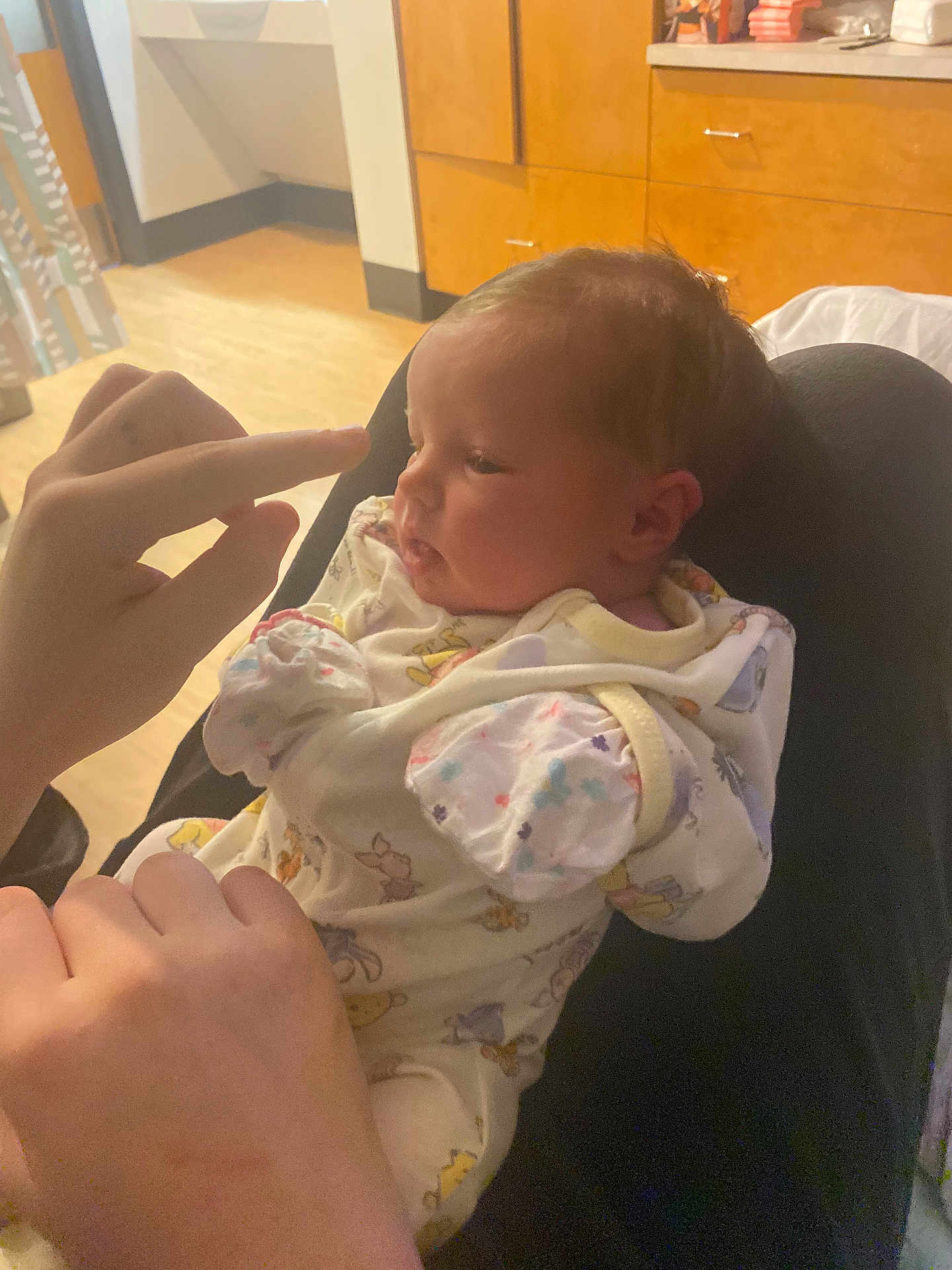 April is registered to the contest to win money with this photo: baby, infant, person, hand, onesie, clothing, fingers, lap, indoor, wooden_cabinet, curtain, floor, light, face, newborn, cozy, soft_lighting, room, portrait, child
