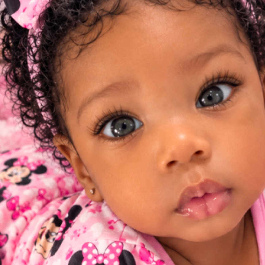 Za'Liyah joined the competition — help win amazing prizes! baby, child, portrait, close_up, curly_hair, bow, headband, pink_clothing, minnie_mouse, cartoon_character, wide_eyes, brown_skin, earring, infant, indoor, photograph, smartphone_screenshot, browser, curious, face