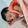 Za'Liyah is registered to the contest to win money with this photo: baby, sleeping, infant, portrait, pink_blanket, soft_blanket, bed, bedding, newborn, peaceful, resting, curled_up, closed_eyes, dark_hair, orange_clothing, white_surface, cozy, indoors, photography, face