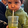 beverage, blue_eyes, candid, casual_clothing, child, closeup, cup, curious, drink, face, green_smoothie, hand, holding, indoor, person, portrait, smoothie, straw, sweater, toddler