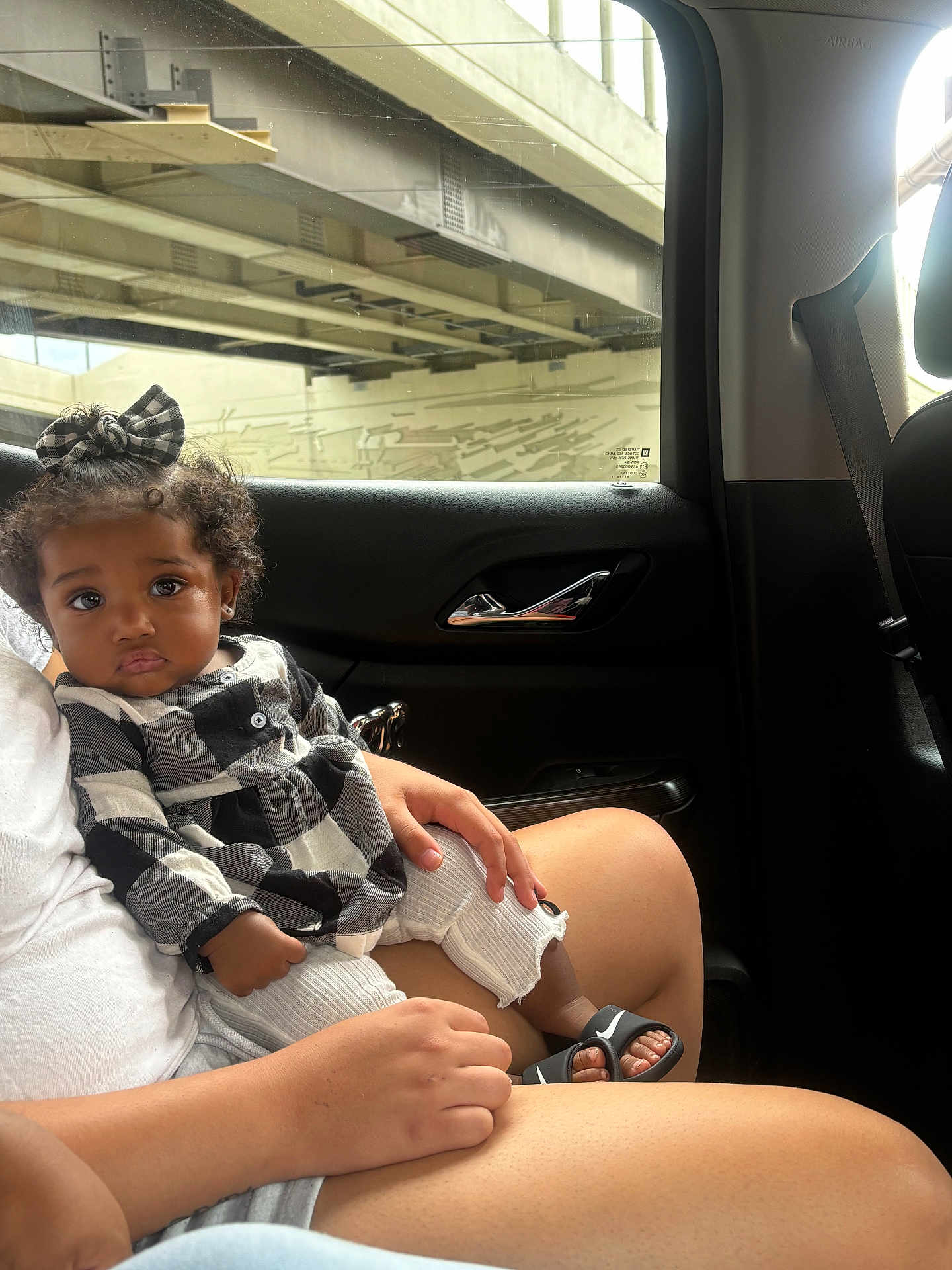 Adore joined the competition — help win amazing prizes! toddler, child, car_interior, window, curly_hair, bow, black_and_white_clothing, sandals, person, lap, hand, seatbelt, door_handle, skin, legs, casual, sitting, portrait, indoors, daylight