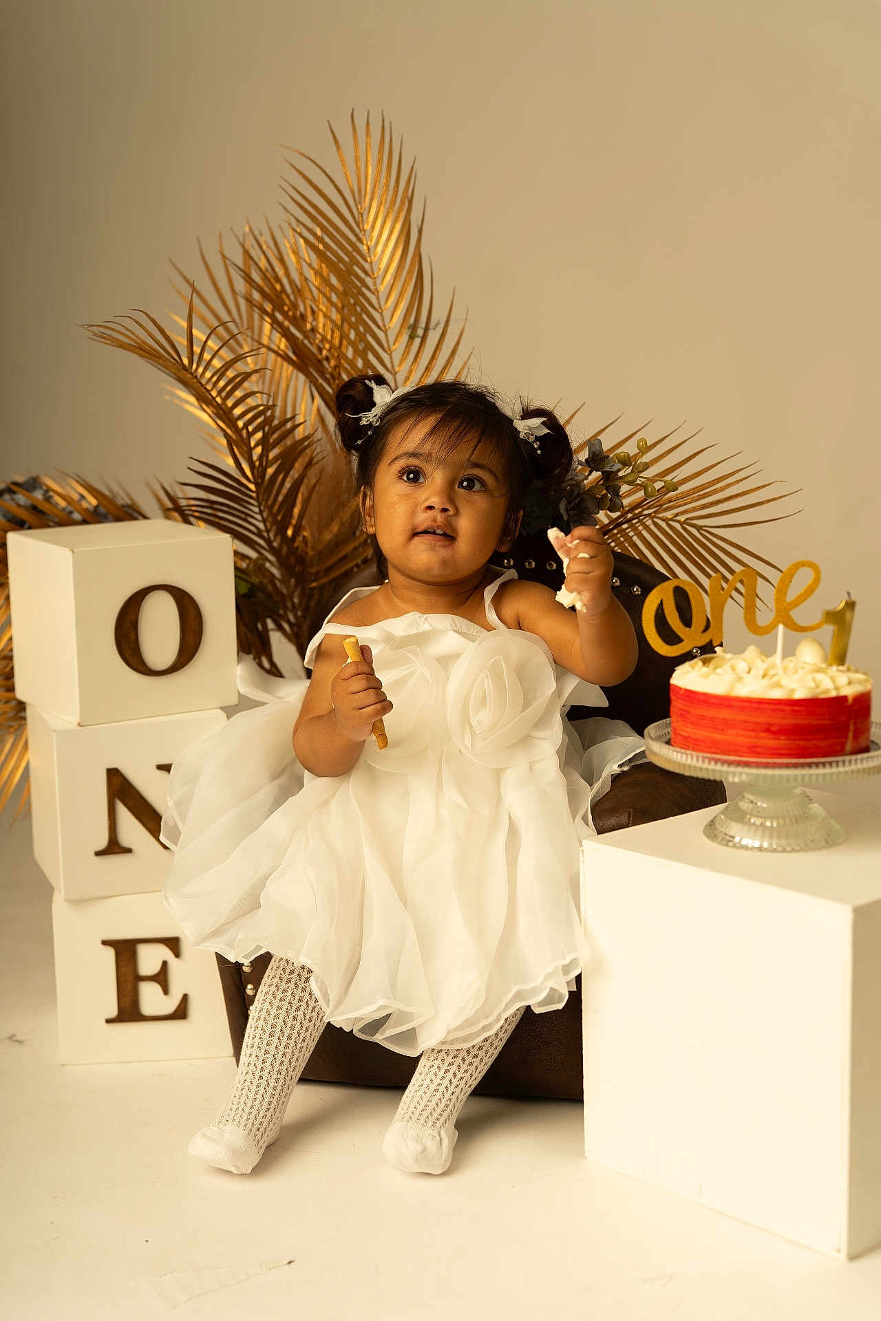 Avleen a rejoint le concours — aidez-le/la à gagner de superbes lots ! toddler, child, white_dress, birthday_cake, cake, snack, decorative_blocks, one, chair, golden_palm_leaves, studio_photo, celebration, party, portrait, cute, happy, indoor, sitting, food, festive