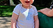 Franklin is registered to the contest to win money with this photo: baby, child, smiling, outdoor, sunlight, grass, building, hand, person, happy, clothing, camo_pants, white_shirt, face, head, portrait, standing, daylight, residential, support