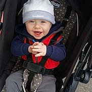 Franklin is registered to the contest to win money with this photo: baby, child, smiling, hat, jacket, stroller, seatbelt, clothing, hands, happy, face, person, outdoor, polka_dot, fabric, baby_wear, casual, cute, blue_eyes, infant