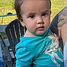 toddler, child, baby, portrait, sitting, outdoor, backyard, patio, chair, bow, hair_accessory, teal_clothing, long_sleeves, person, face, eyes, serious_expression, adult, sunlight, suburban_house