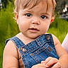 baby, child, infant, portrait, face, eyes, looking_at_camera, denim, overalls, clothing, outdoor, garden, greenery, natural_light, close_up, sitting, hands, blond_hair, blue_eyes, smiling