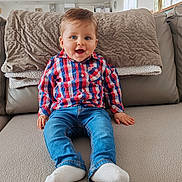 Marceau a rejoint le concours — aidez-le/la à gagner de superbes lots ! baby, child, smiling, sitting, blue_eyes, plaid_shirt, jeans, white_socks, couch, blanket, indoor, cozy, happy, portrait, person, furniture, home, casual_clothing, infant, natural_light