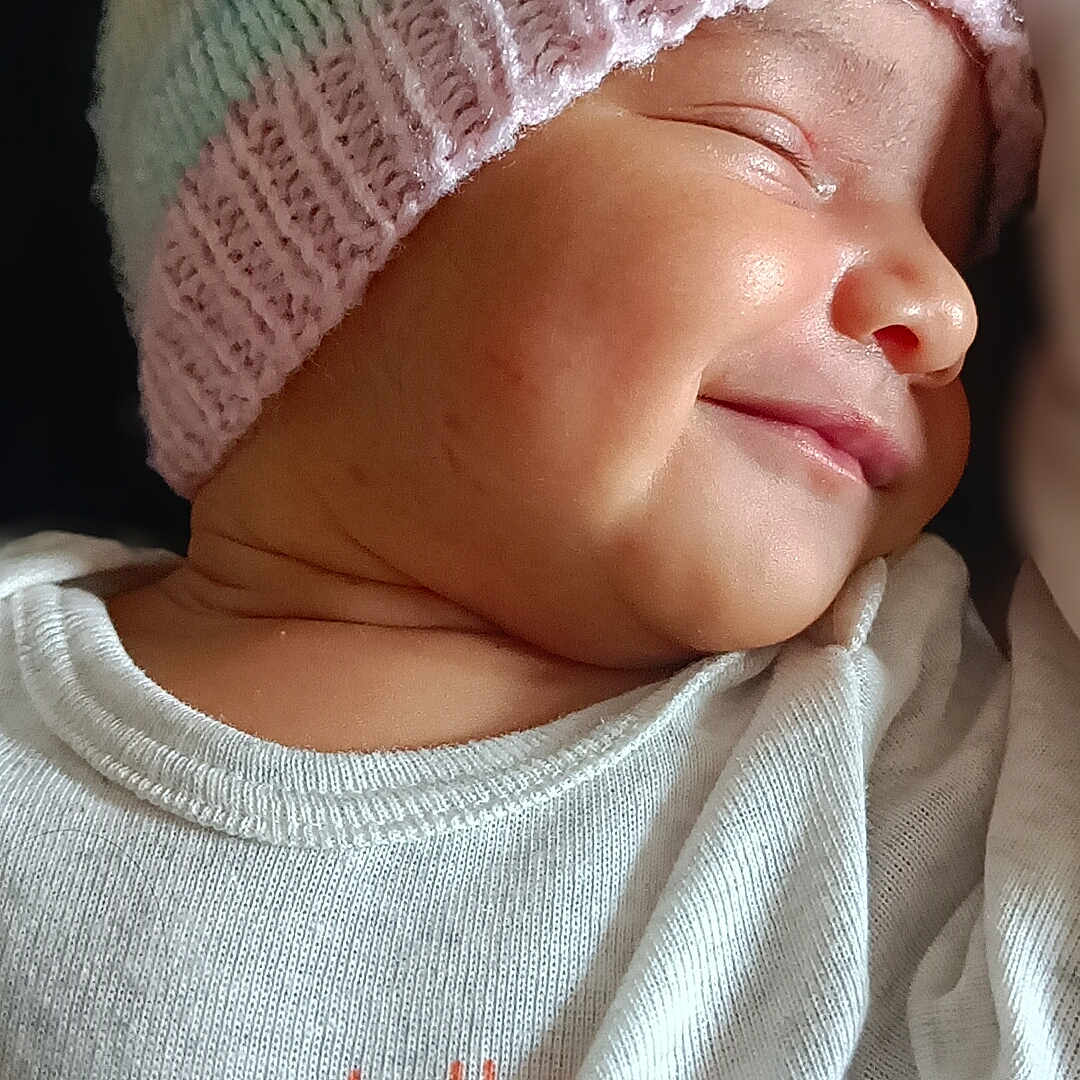 Anaya is registered to the contest to win money with this photo: apparel, baby, baby_clothes, child, closeup, cute, dark_background, face, headwear, infant, knit_hat, pastel_colors, peaceful, portrait, pumpkins, skin, sleeping, smiling, soft_light, white_shirt