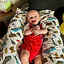 James is registered to the contest to win money with this photo: baby, infant, smile, red_onesie, pillow, landmark_print, couch, sock, happy, face, indoor, person, child, cute, comfort, fabric, home, relaxing, colorful, portrait