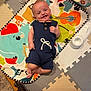 baby, smiling, romper, play_mat, colorful, musical_instruments, animal_print, indoors, floor_mat, happy, child, infant, person, cute, small, lying_down, toy, playtime, joyful, cozy