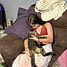 blanket, cat, couch, cozy, cuddling, girl, indoor, long_tail, necklace, person, pet, pillow, red_top, relaxed, sitting, sleeping, sofa, striped_fur, tabby_cat, tattoo