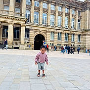 Gursher is registered to the contest to win money with this photo: child, building, plaza, urban, people, walking, historic, architecture, outdoor, casual_clothing, hoodie, shorts, sandals, pavement, daytime, city, tourists, crowd, smiling, playful