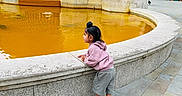 Gursher joined the competition — help win amazing prizes! child, fountain, orange_water, hoodie, shorts, sandals, side_view, curious, urban, stone, architecture, pavement, outdoor, daylight, young_child, person, building, reflection, city, casual_clothing