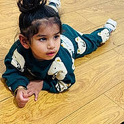 Gursher is registered to the contest to win money with this photo: child, toddler, floor, wood_floor, clothing, sweatshirt, pants, bear_pattern, hair_bun, curly_hair, indoors, casual, cute, playful, young_child, feet, shoes, skin, portrait, contemplative