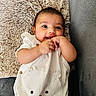 baby, infant, smiling, cute, pillow, couch, clothing, striped, face, hand, playful, happy, indoor, portrait, person, child, soft_texture, fabric, cozy, resting